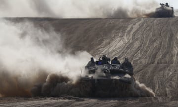 Clouds of dust and dirt fly up as armoured vehicles drive through a barren landscape