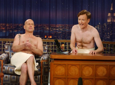 two men wearing just towels - bruce willis sits in guest armchair and conan sits behind desk
