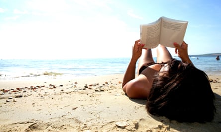 Picture of a woman in a swimsuit laying on a sandy beach reading a book
