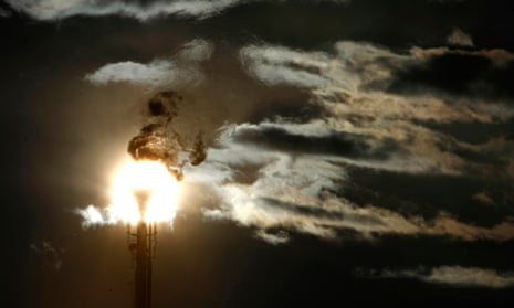 A flare stack emitting fire is silhouetted against the sun at an oil refinery in Melbourne