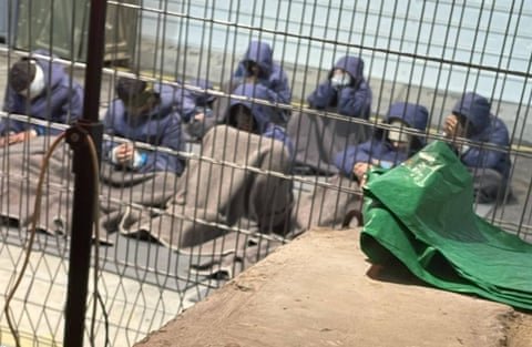 Blurry image of people sitting on the ground behind a metal barrier