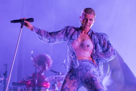 Robyn in a purple outfit sticks her tongue out while performing on stage.