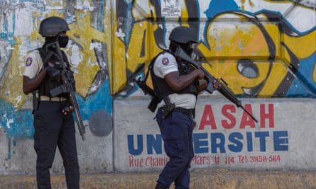Police officers carrying rifles stand in front of graffiti in Port-au-Prince