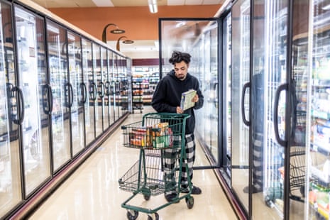 A man in a grocery store freezer aisle putting a frozen food item in his cart