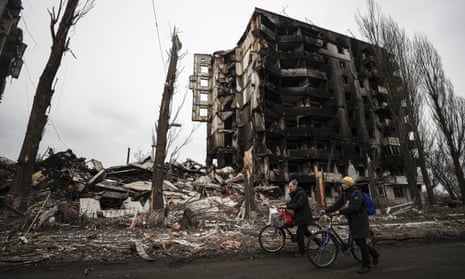 Ukrainians push bicycles for transportation near the ruins of damaged buildings in Borodianka