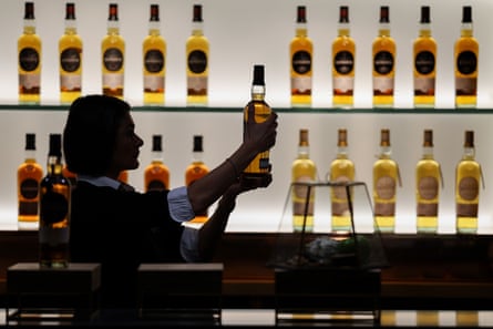A silhouetted figure holds up a whisky bottle, in front of a display of bottles on shelves