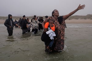 A woman wades through the water holding her child and throwing out her arm as she calls out