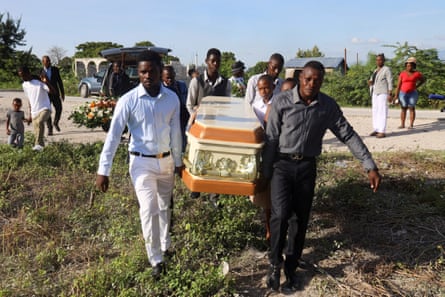 About eight men in dress shirts and pants carry a casket across a dry field.