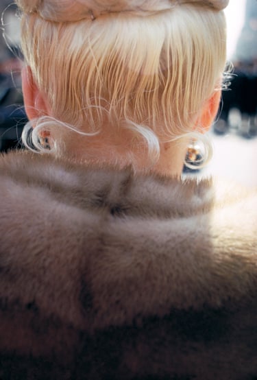 A photo of the back of a woman’s head - she has blonde hair and is wearing a fur coat