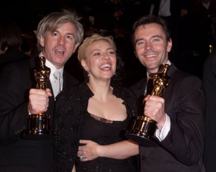 In evening dress, two men clutch Oscar statuettes while a woman wearing a black dress smiles broadly