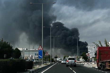 Motorists drive past a plume of smoke rising from a reported Iranian strike in the industrial district of Doha on 1 March 2026.