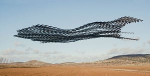 A flock of birds drawing a long, sinuous shape over a desert landscape