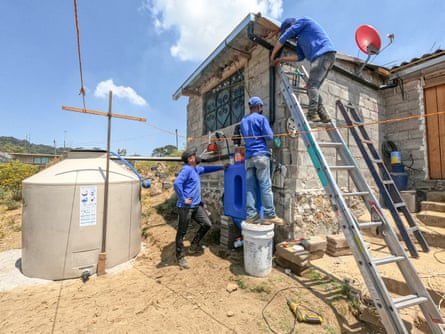 Men in blue overalls, one up a ladder, installing a rainwater harvesting system outside Mexico City.