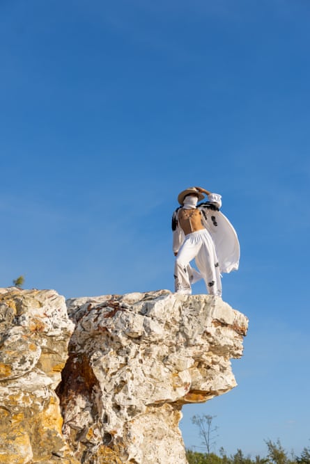 A man wearing white stands on a rock in front of a blue sky