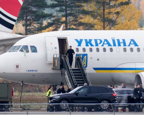 President Zelensky descends aircraft stairs beside a plane marked "Ukraine", with vehicles waiting below