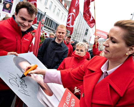 Mette Frederiksen signs an election poster of herself as people look on behind.