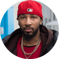 Man with beard and goatee, red baseball cap on backwards, red shirt, puffy coat, gold chains
