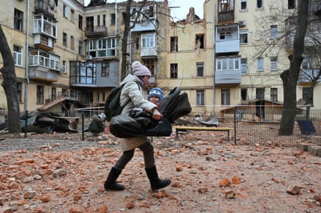 A local resident carries her baby outside their residential building partially destroyed after a missile strike in Kharkiv.