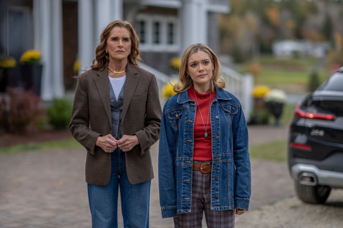 Two women stand side by side on a driveway looking concerned