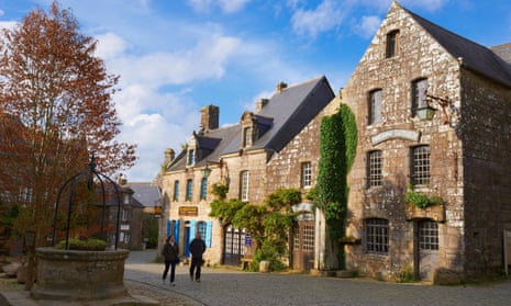 Two people walking through Locronan village in Brittany, past old stone buildings.