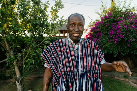 An older black man in a bright patterned shirt smiling in a garden