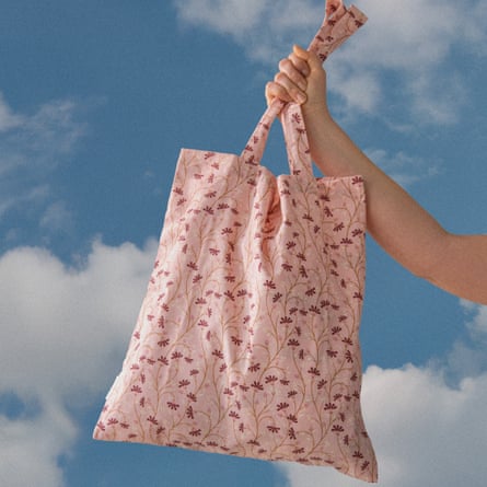 A hand holds a pink patterned bag up against a blue and white-cloud dotted sky