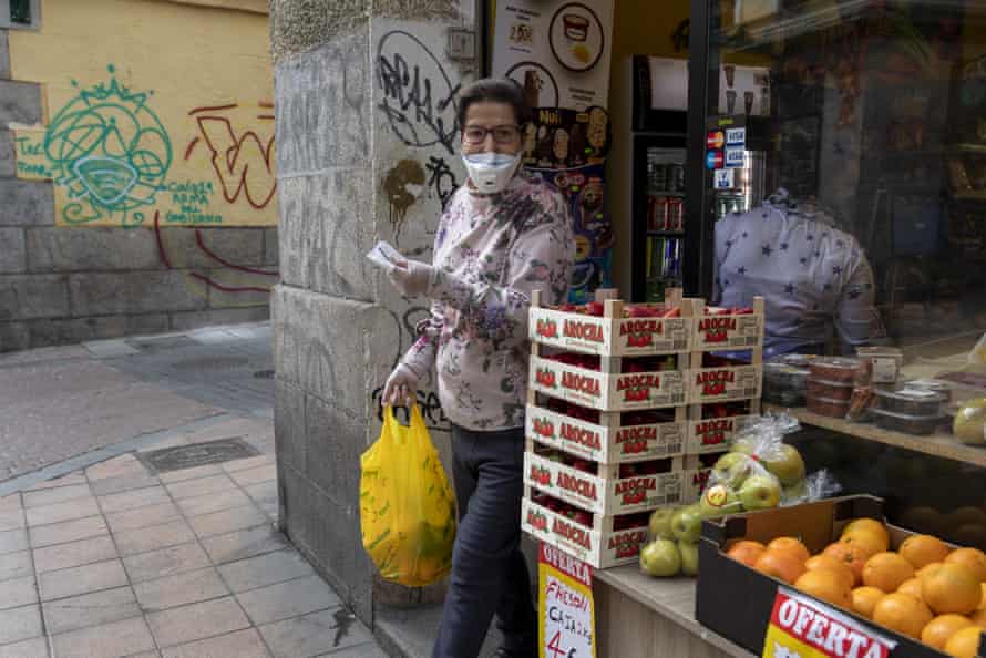A woman leaves a fruit store in Madrid wearing a protective mask and gloves