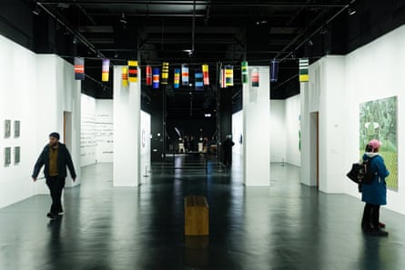people are looking at paintings on the walls and small, brightly coloured flag-like emblems hang from the ceiling.