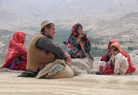 A man and his wife and three daughters sit on a roadside overlooking a valley