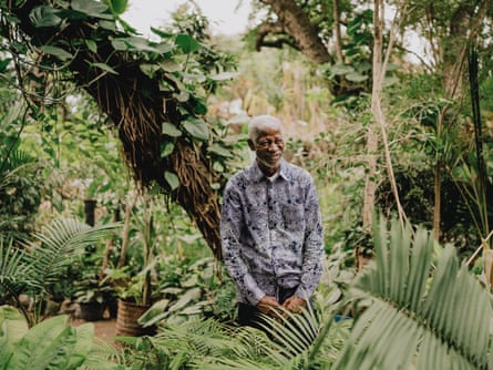 A man stands with his back to a vine-covered tree, surrounded by greenery.