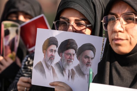 A woman holds an image depicting the late founder of the Islamic Republic, Ayatollah Ruhollah Khomeini, slain supreme leader Khamenei, and current supreme leader Mojtaba Khamenei.