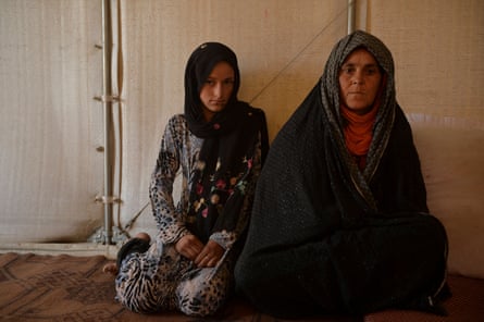 A girl and a woman wearing headscarves sit on the floor