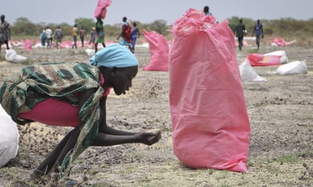 A woman scoops up fallen grain after an aerial food drop by the World Food Programme in Kandak, South Sudan.