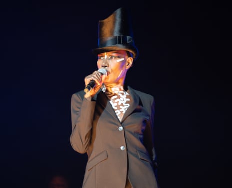 Grace Jones in silk top hat, black dinner jacket, with white stripes on face and white cogwheels painted on her skin possibly