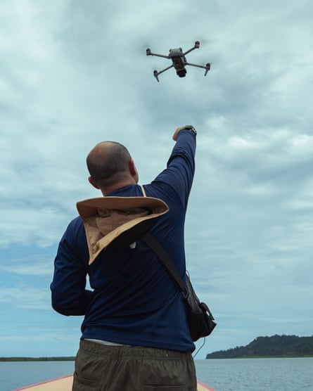 A man seen from behind attempts to catch a drone flying just above him