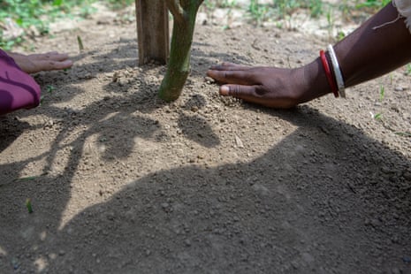 A hand smooths over earth on a newly planted plot.