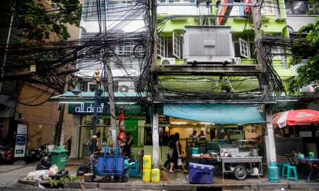 A clutter of overhead telecommunications lines above a street food vendor's stall in Bangkok, Thailand