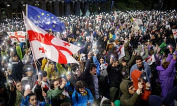 A big crowd of protesters holding Georgian and EU flags in a street at night