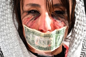 A woman at a protest with a dollar bill over her mouth