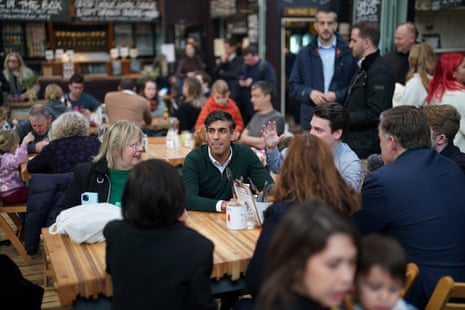 Sunak sits at a table with several other people in a cafe area