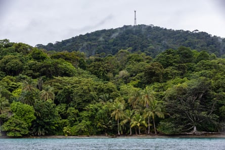 A heavily forested tropical island with a radio tower on a hill in the distance