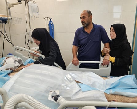 Alaa al-Najjar stands next to her husband who is lying in a hospital bed