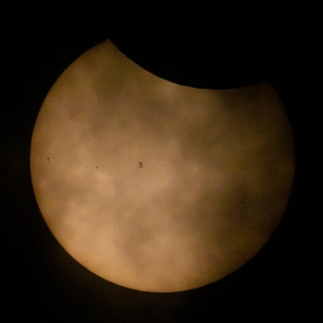 The Sun during a partial solar eclipse and partially obscured by clouds, the International Space Station silhouetted as it transits at roughly five miles per second.