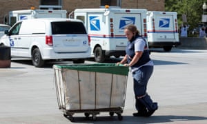 A United States Postal Service (USPS) worker pushes a mail bin outside a post office in Royal Oak, Michigan, this summer.