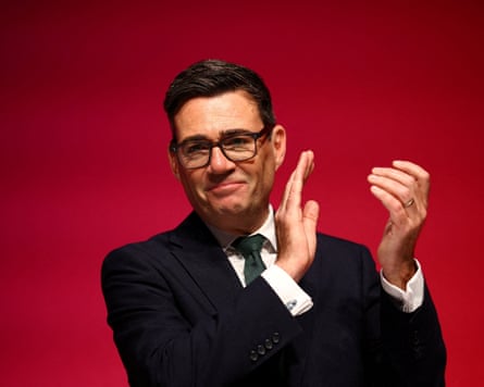 Andy Burnham applauds to a red background.
