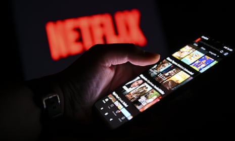 main page of 'Netflix' is displayed on a smart phone screen in front of a screen displaying the logo of 'Netflix'
