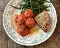 A plate with ricotta and breadcrumb polpette in tomato sauce, green beans, and bread.