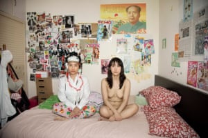 Two women, one naked, sit on a bed