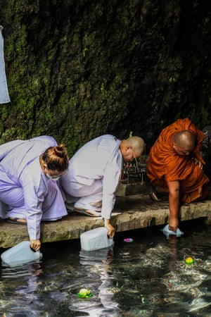 Buddhist monks collecting water from a stream using plastic containers