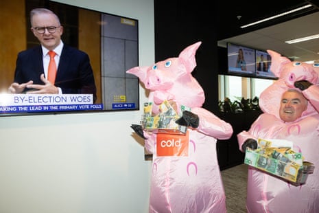 Two men dressed in pig suits by a TV of the prime minister
